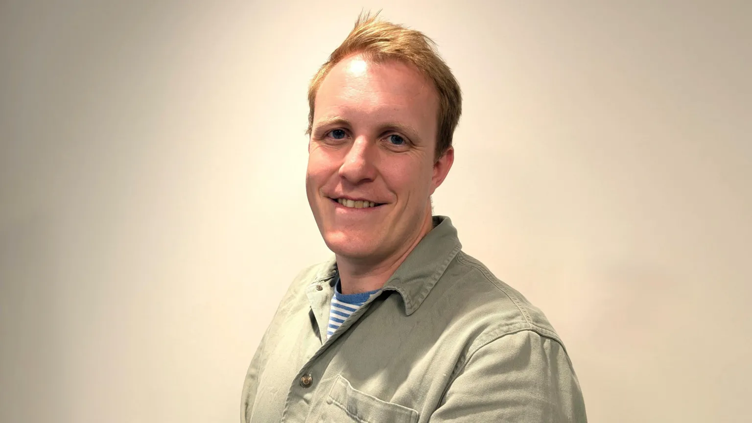 Steffan Evans A young man with short blonde hair, smiling and wearing a light brown shirt.