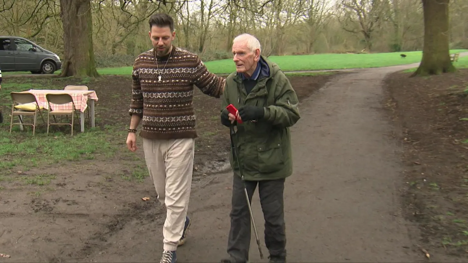 Diaco and Brian walk through the park, Brian has a walking stick, and Diaco has his arm round his back