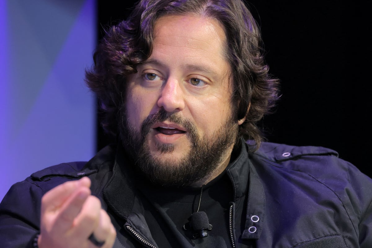 A bearded man with longish hair speaks and gestures.