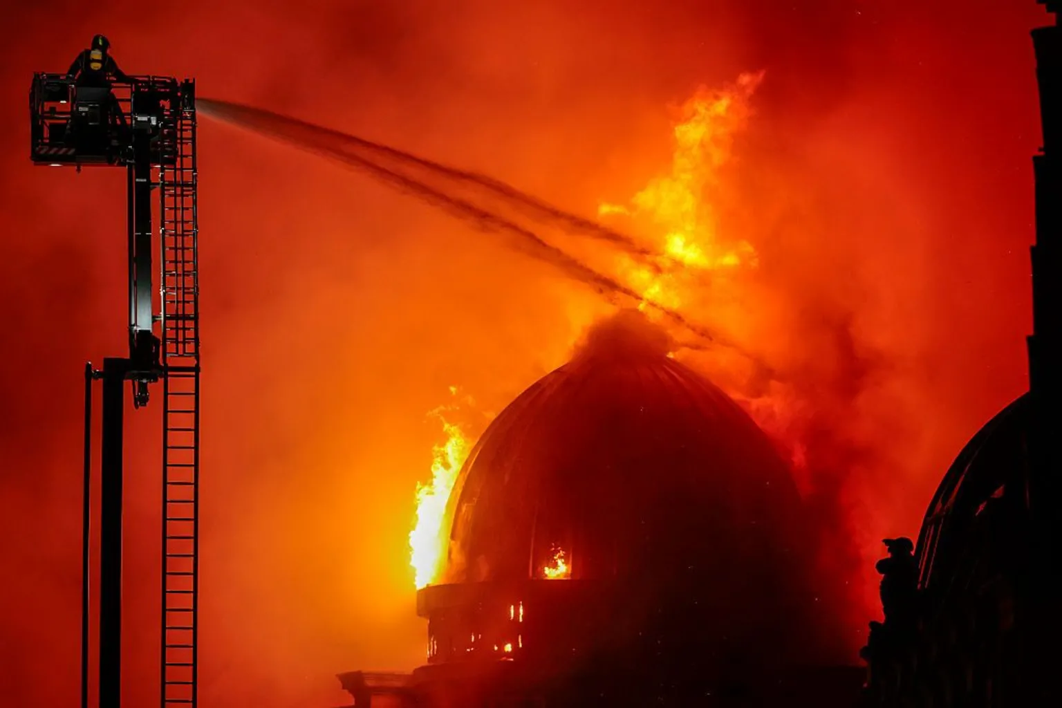 Huge fire with dome burning. The whole sky is orange and fire fighters are spraying water on the building