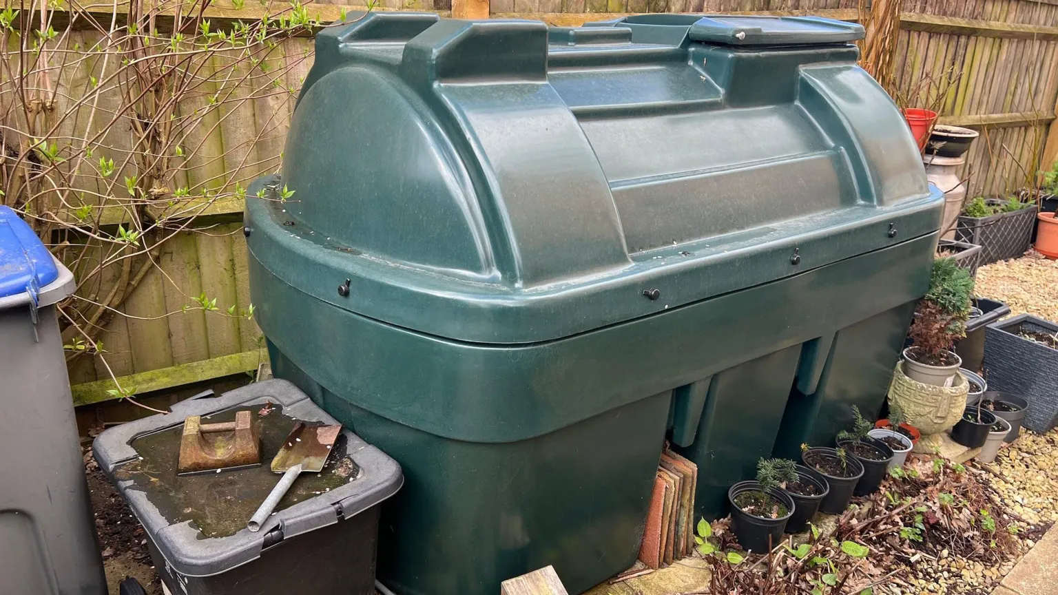 A large dark green plastic heating oil container in a garden