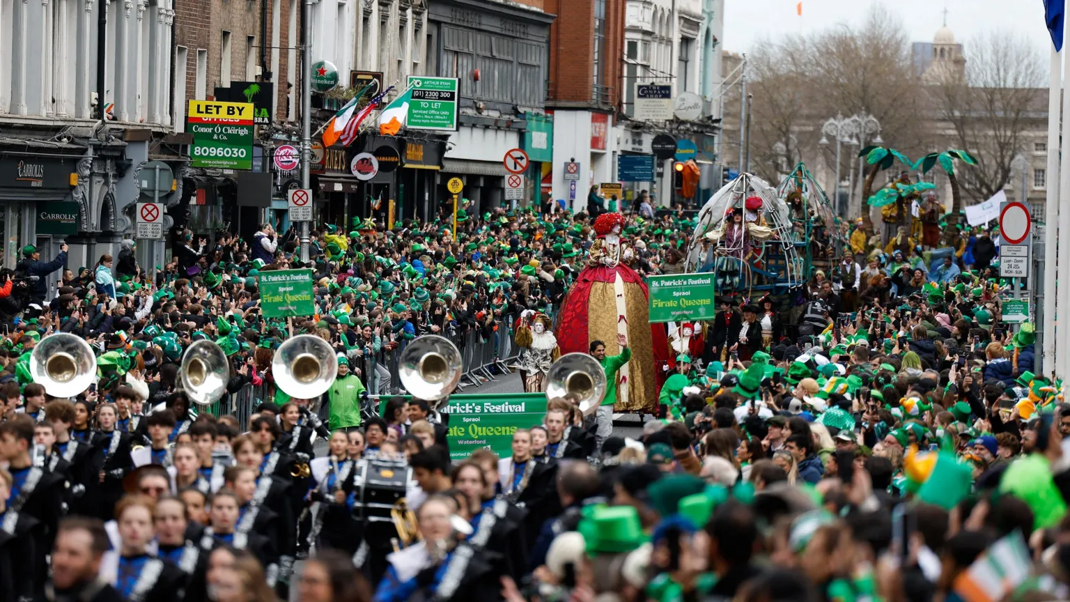  Crowds gathered in Dublin for St Patrick's Day parade. Floats are making their way down with street with bands playing large brass instruments.
