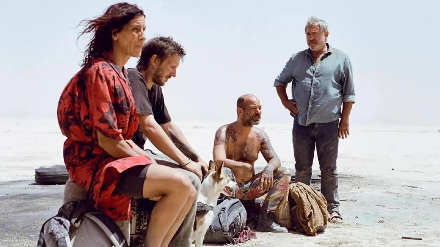 Quim Vives A promotional still image from the film Sirat showing four people sitting in the desert