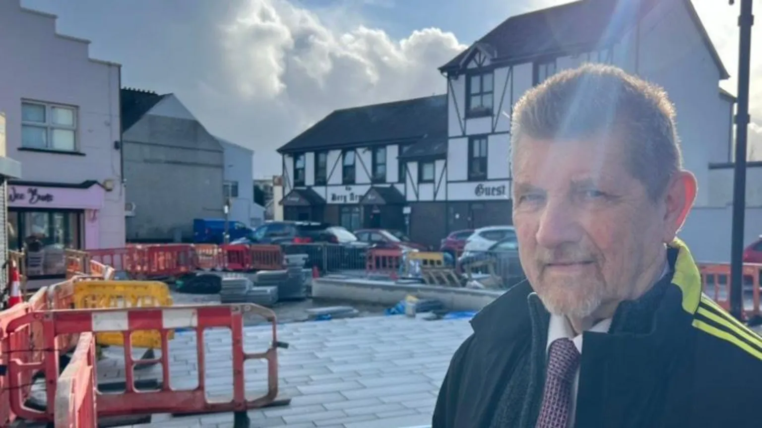 A man standing wearing a jacket. Behind him is construction works.