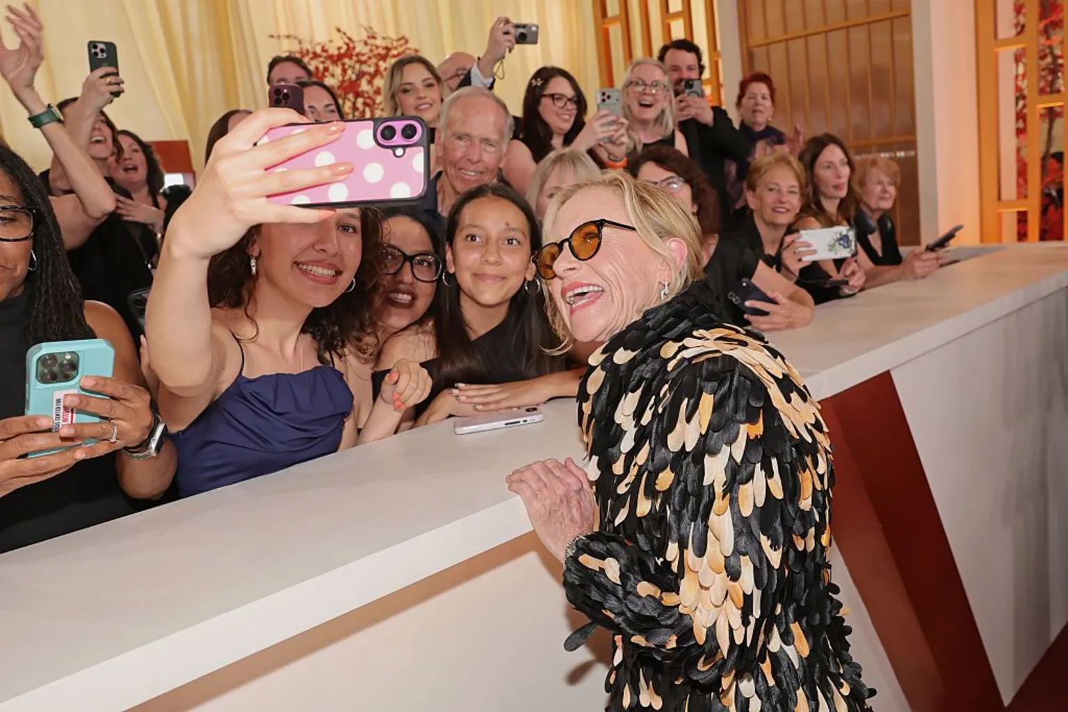  Amy Madigan poses for a selfie with people behind a partition on the 98th Oscars red carpet at the Dolby Theatre 