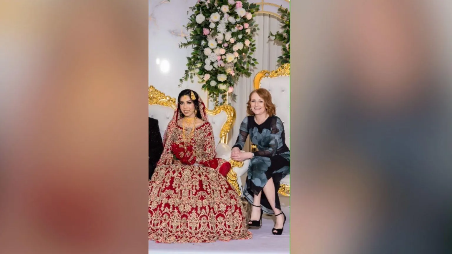 Royal Grafix Two women are sat down smiling. The woman on the left is wearing a red and gold embellished dress and has brown hair. The woman on the right is wearing a black and grey dress with ginger hair.