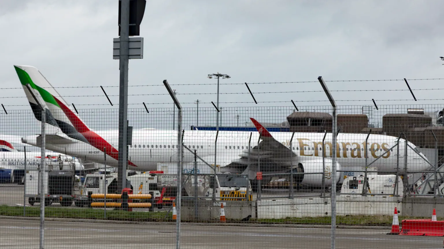 Alan Simpson Emirates plane at Edinburgh Airport. It is behind a metal fence with other planes behind it.