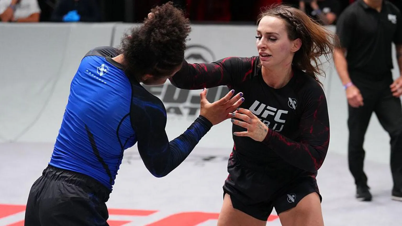  Ffion Davies fighting Cassia Moura. She has her hand on Moura's head attempting a grappling move. She is wearing a black UFC BJJ branded top.