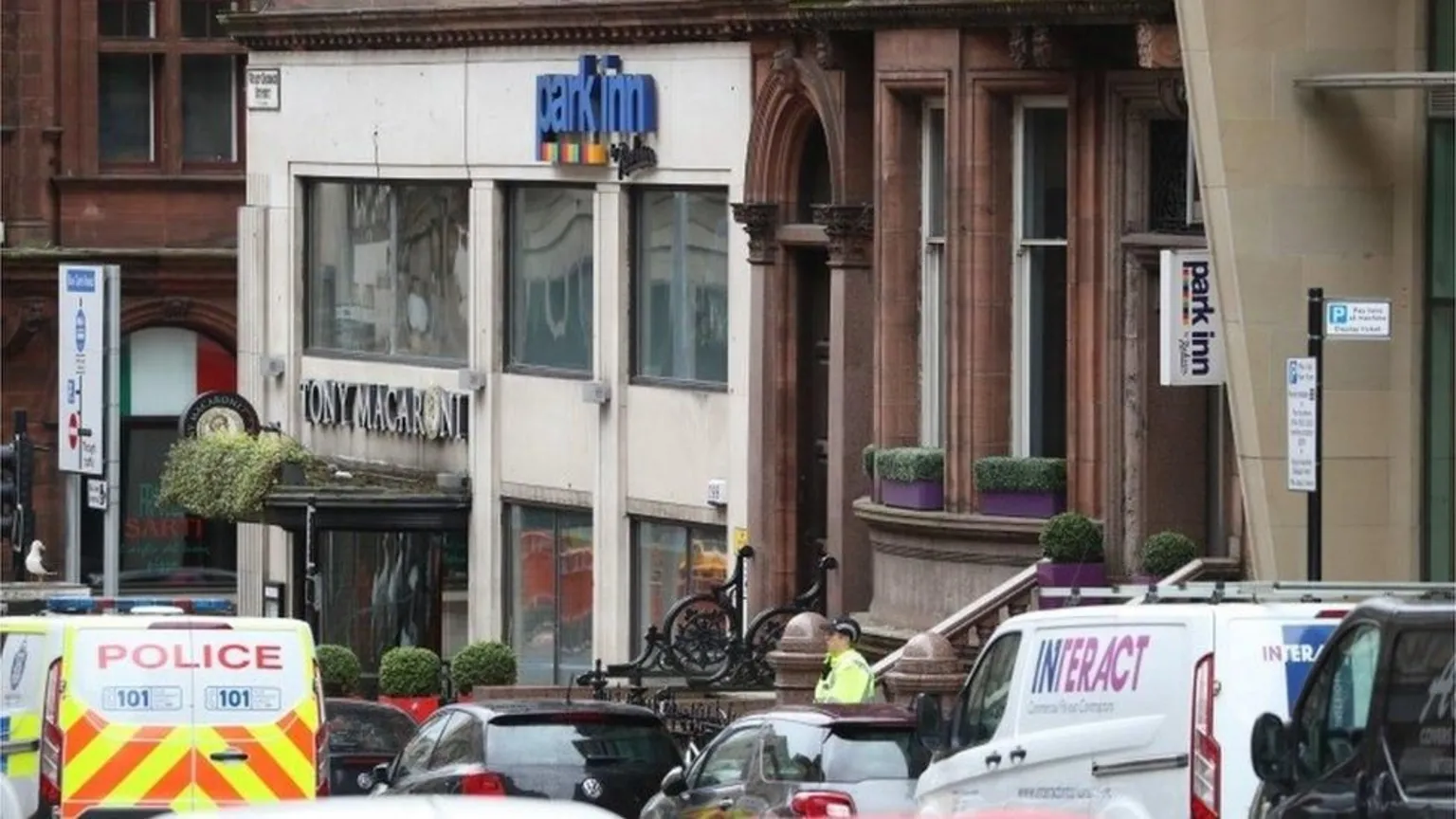  Police vans outside a hotel on a city street. A police officer can be seen standing outside.
