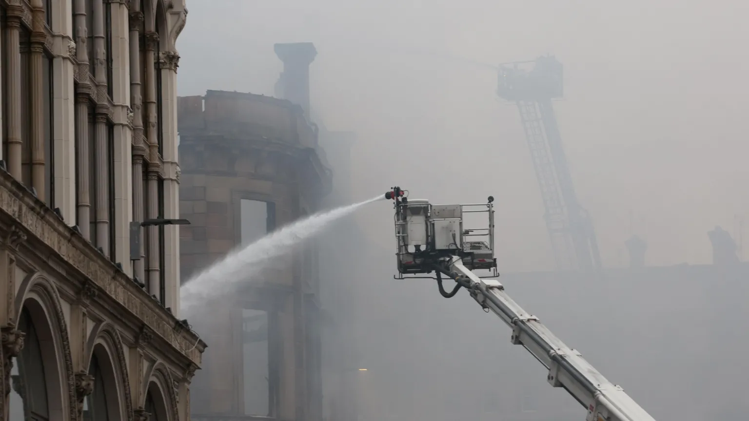 A high-reach appliance spraying water on the remains of the building.