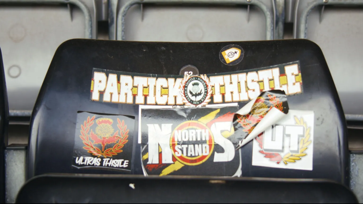 Patrick Thistle Ultras stickers on a seat in Firhill Stadium. The stickers have black, red, yellow and white logos and text.