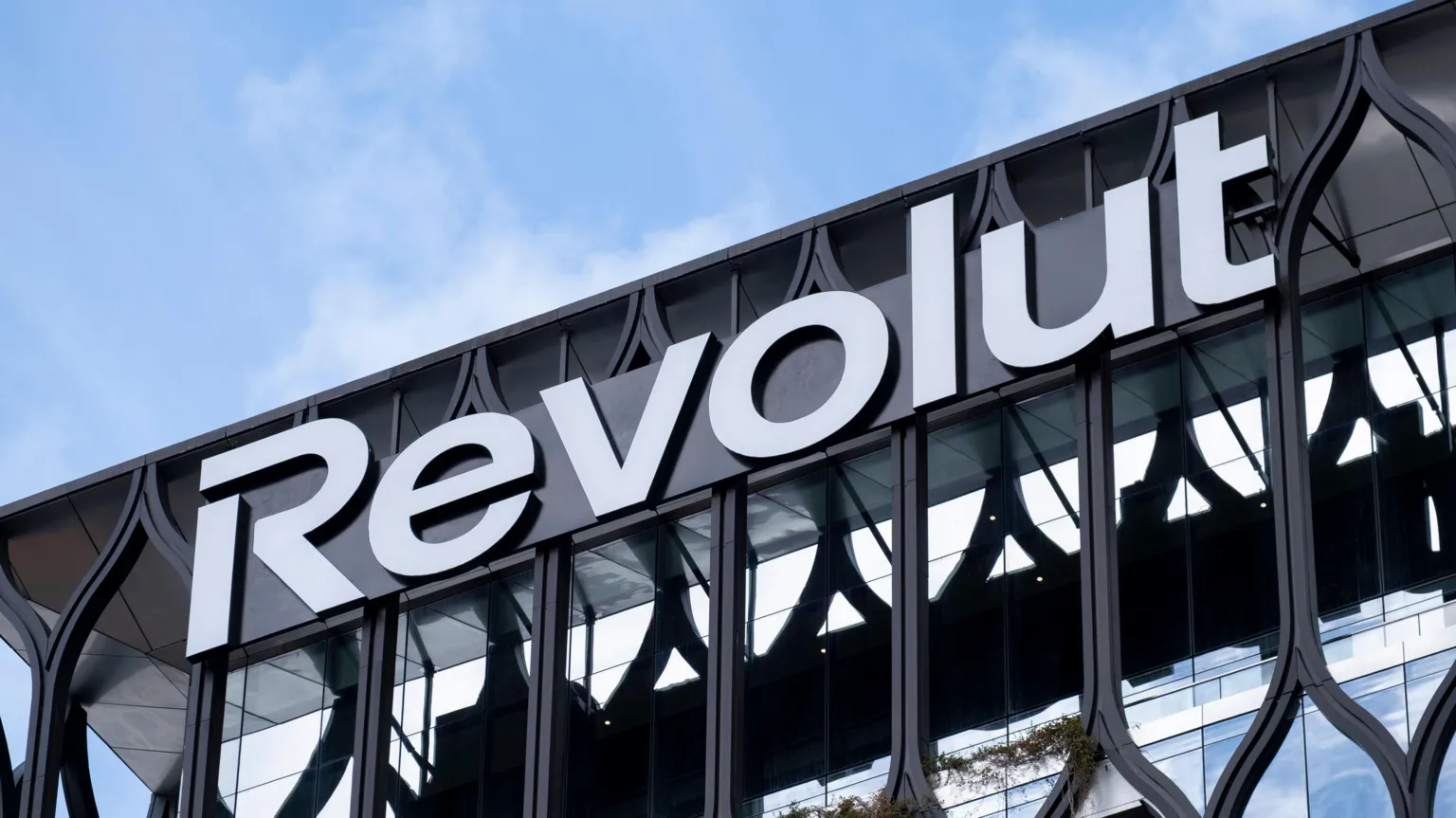 A large glass fronted building with black metal framing sits in front of a blue sky. Writing on the building reads 'Revolut' in large white letters.