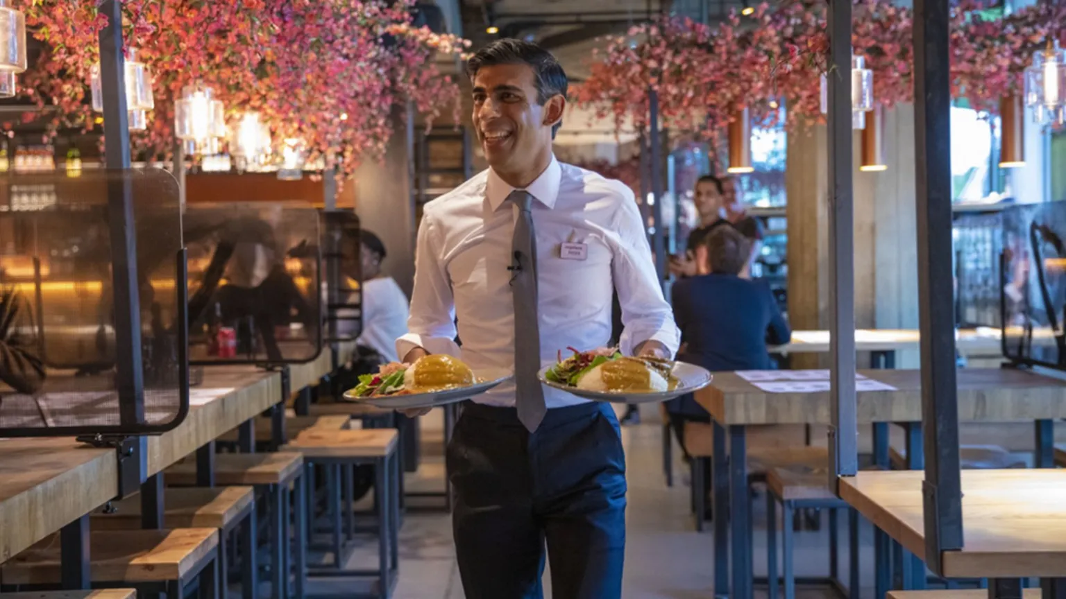 HM Treasury Former Chancellor Rishi Sunak carries two plates of food in a branch of Wagamama's to promote the 