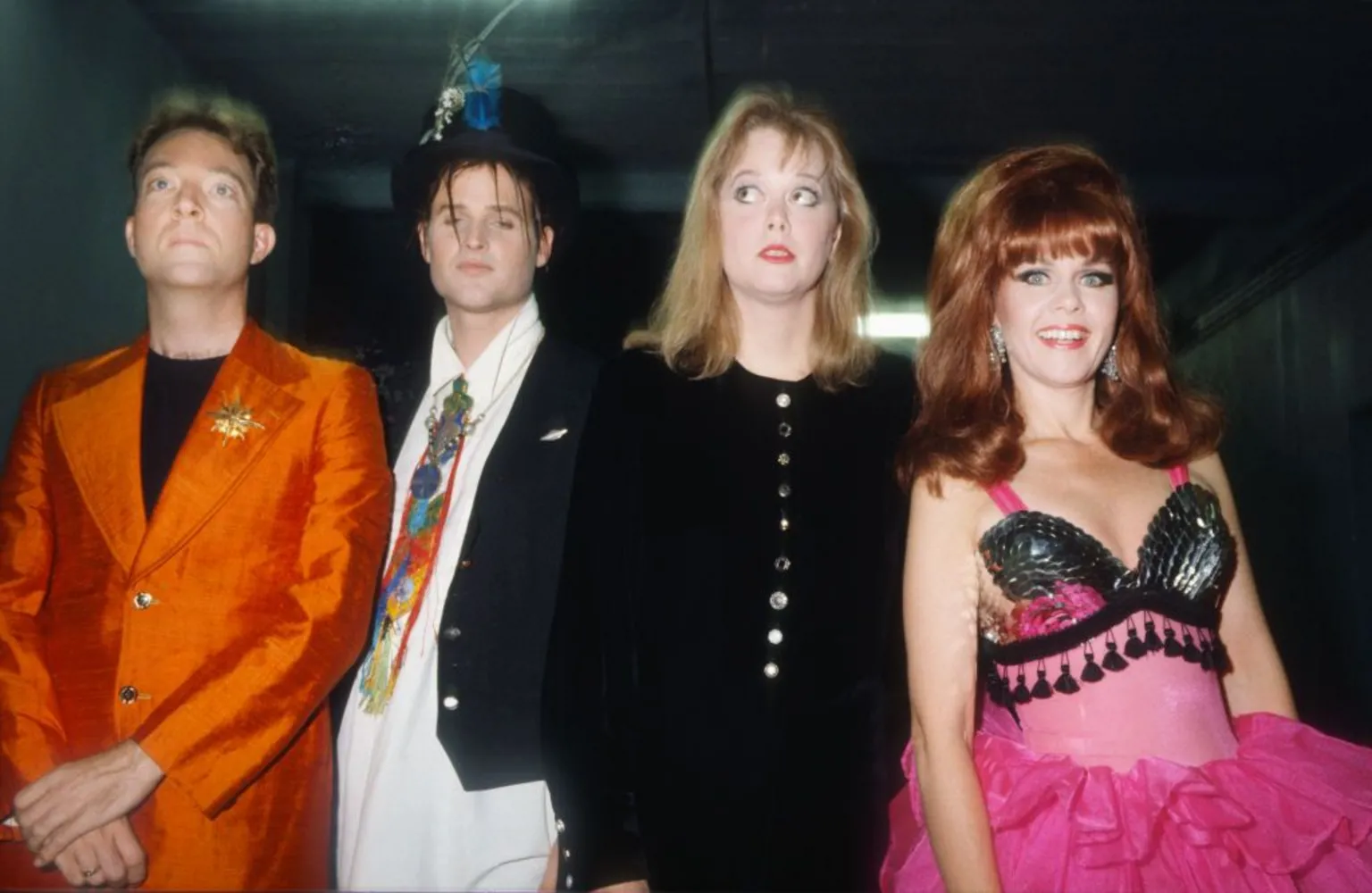  The B-52s pictured backstage at a gig in 1989. Fred Schneider is wearing a striking orange jacket with a gold brooch, while Keith Strickland sports a feathered top hat. Cindy Wilson, in a relatively sober black outfit, glances to the side, while Kate Pierson, in her trademark beehive, is wearing a frilly pink tutu.