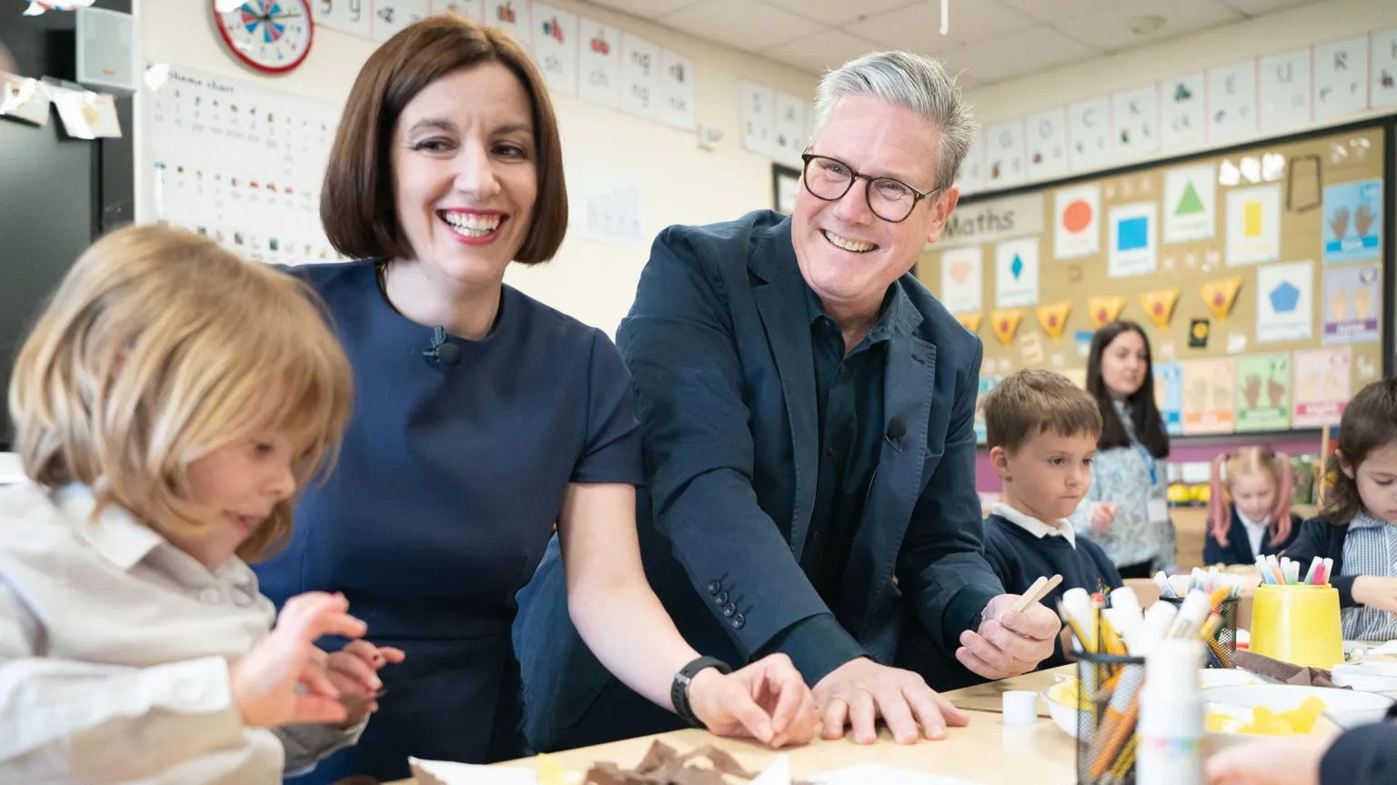  Education Secretary Bridget Phillipson is pictured with Prime Minister Sir Keir Starmer during a visit to Nursery Hill Primary School, in Nuneaton, Warwickshire before the 2024 general election. They are smiling and are surrounded by children who are doing crafts. 
