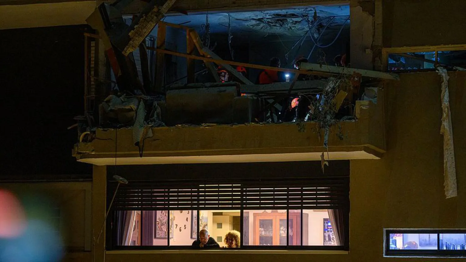  Rescuers work through rubble at the strike site. It is night time and they wear head torches. 