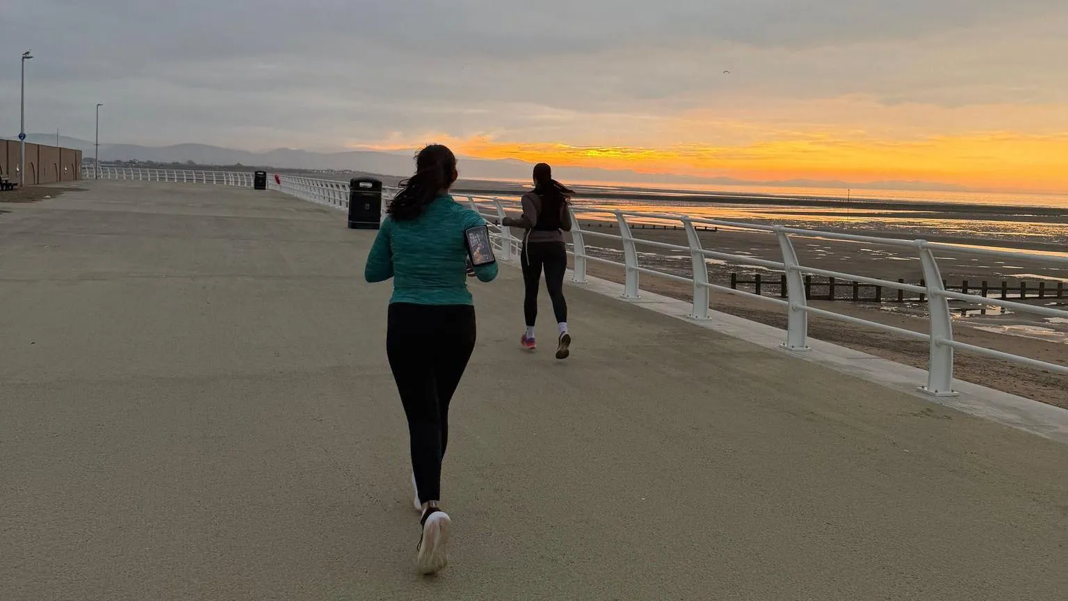 North Wales Police Two women running on Rhyl's coastline in North Wales with a sunset in the background 