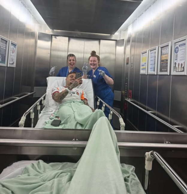 Noa Lang smiling from a hospital bed with two nurses at Whiston Hospital