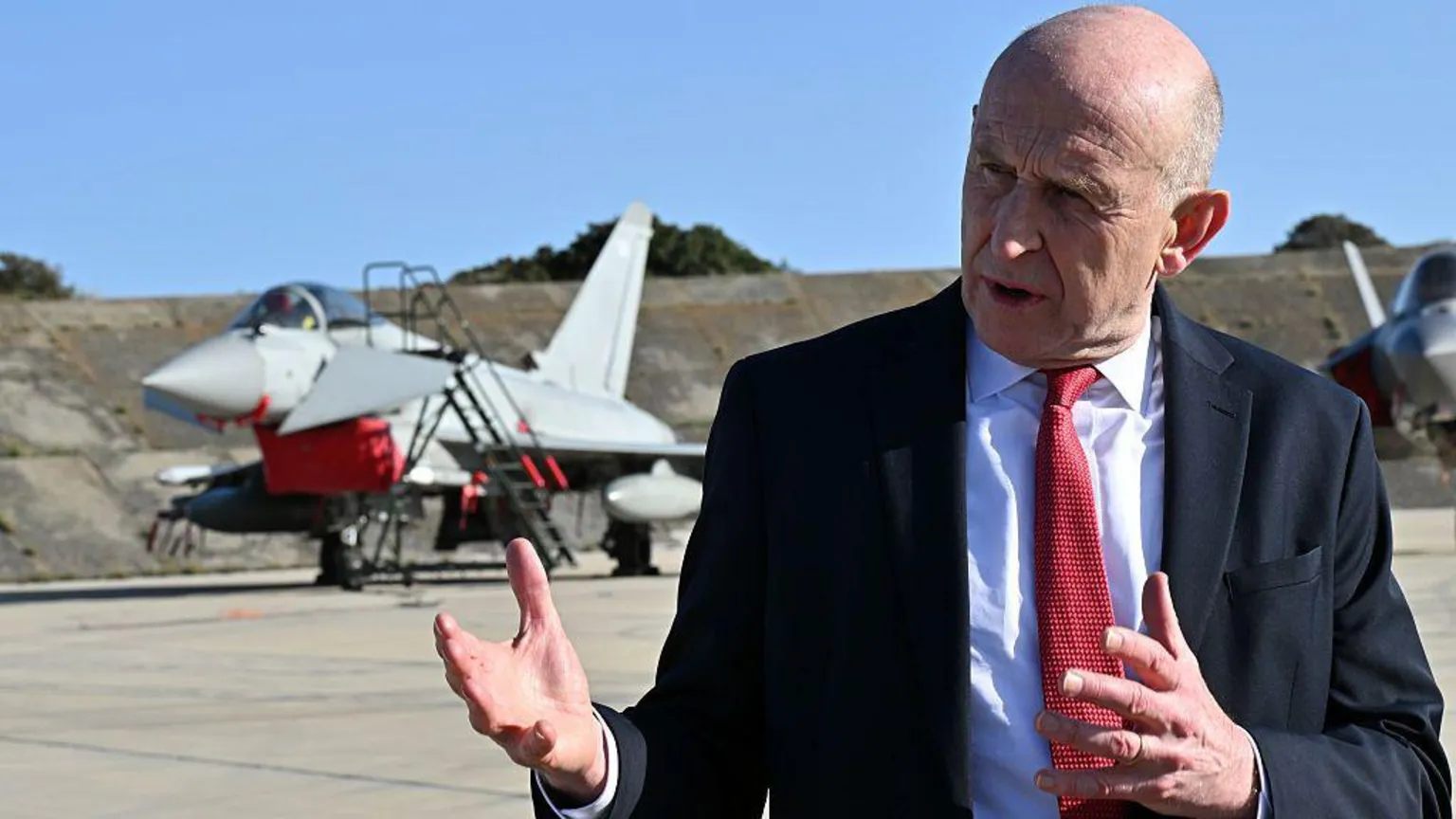 Leon Neal/ A man in a suit stands in front of a UK Typhoon jet