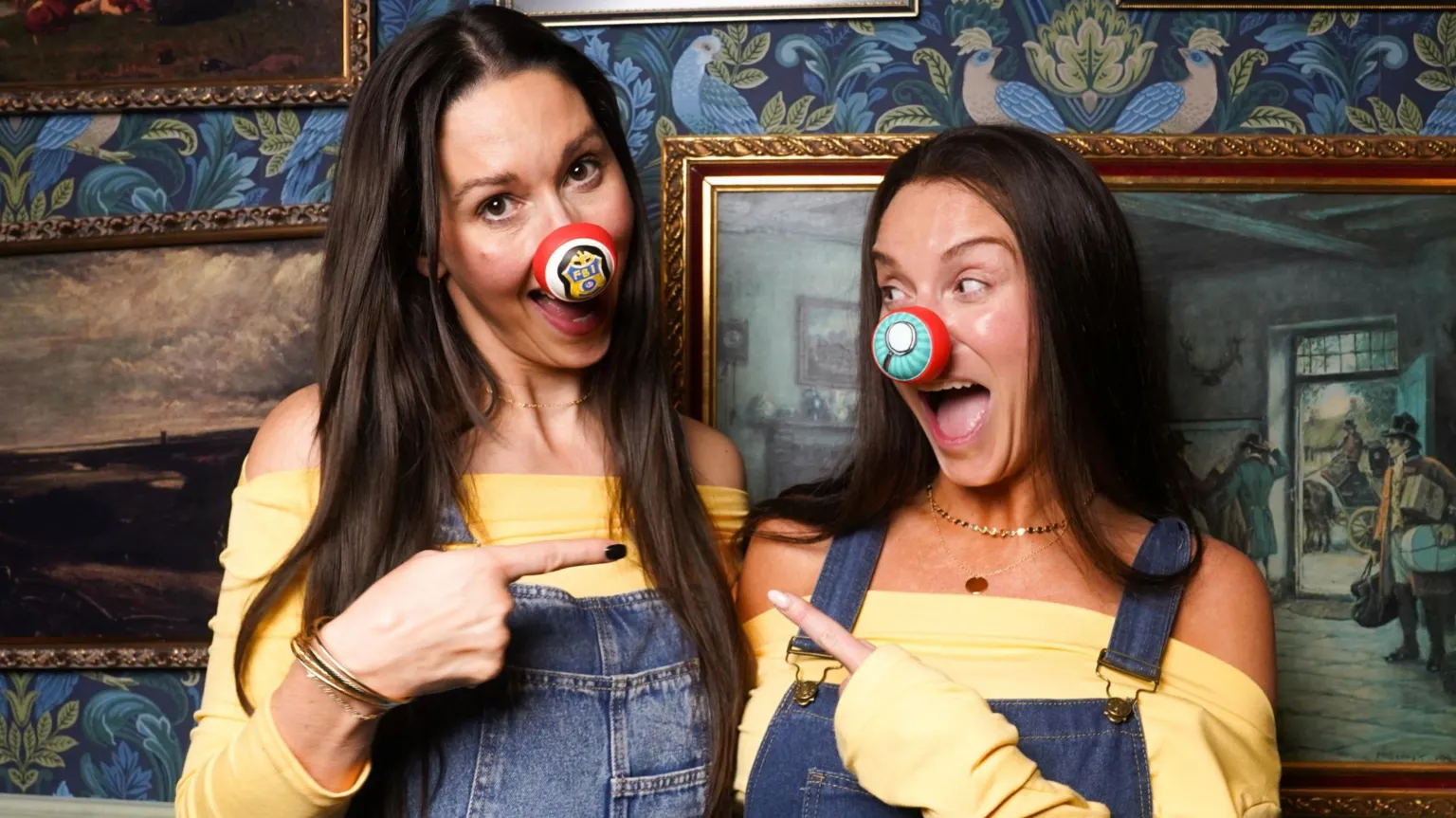  Rachel Duffy and Vicky Pattison wearing matching yellow tops and denim dungareers in front of a panelled wall hung with paintings.