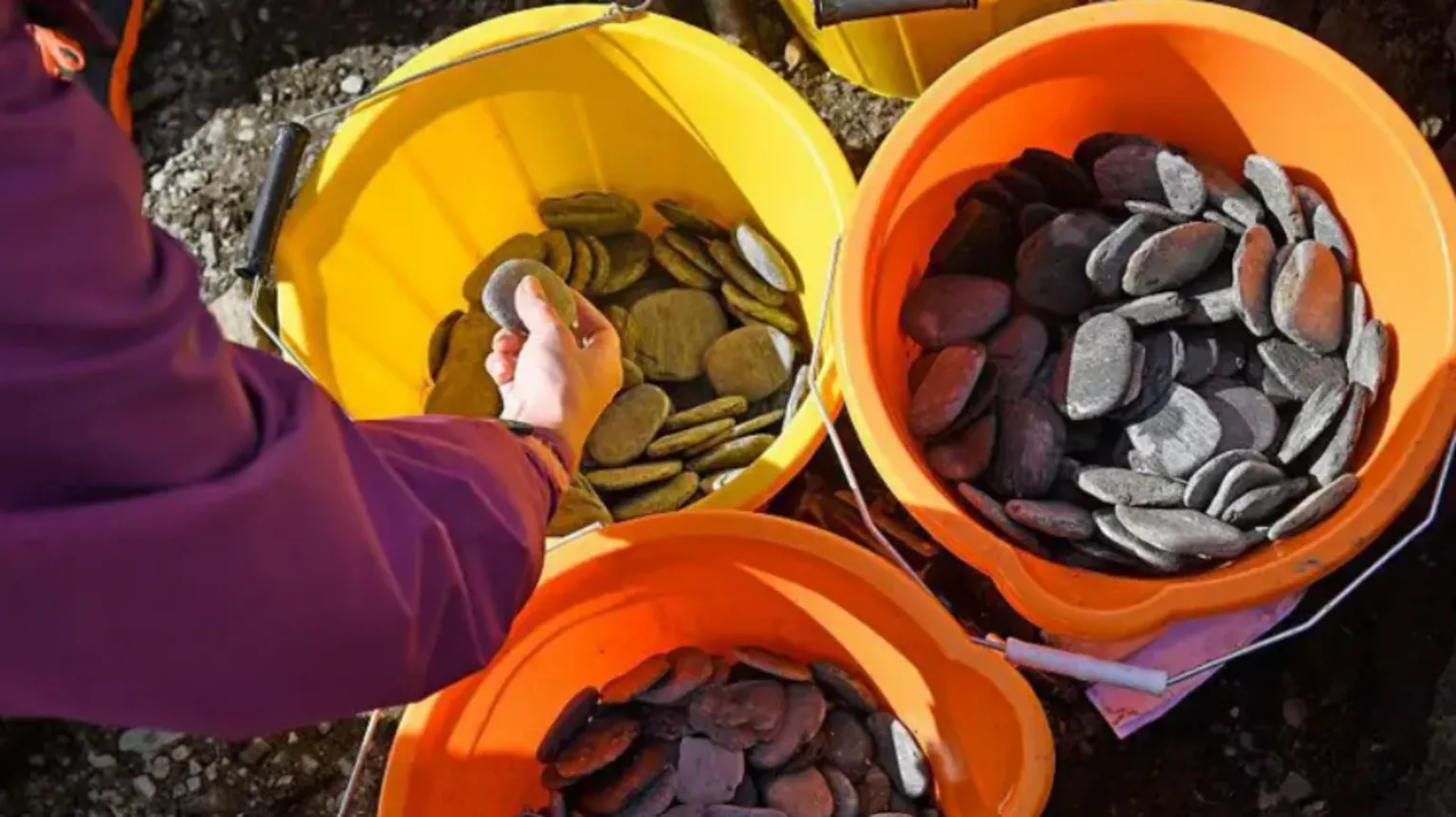 AFP via Shows several bright buckets filled with smooth, flat stones, with a person selecting one from a yellow bucket.