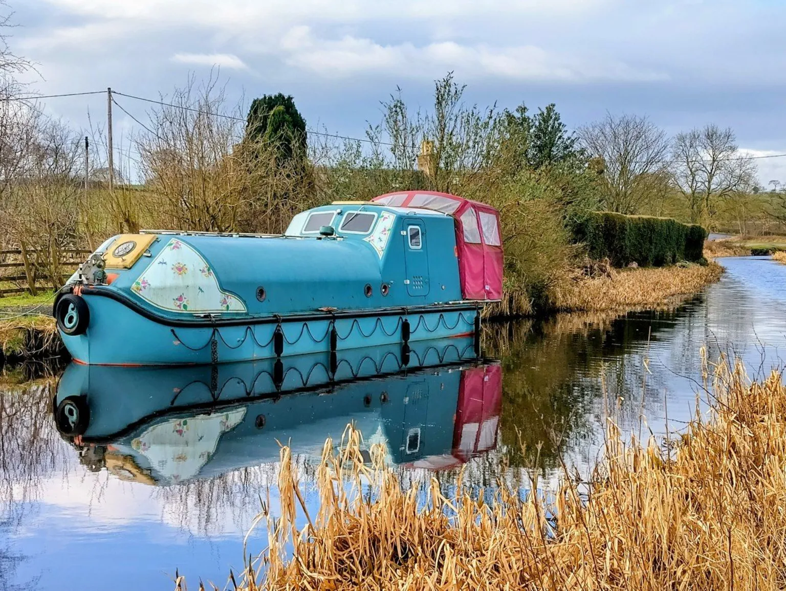 Anne Wheatley A blue and pink narrow boat berthed on a canal