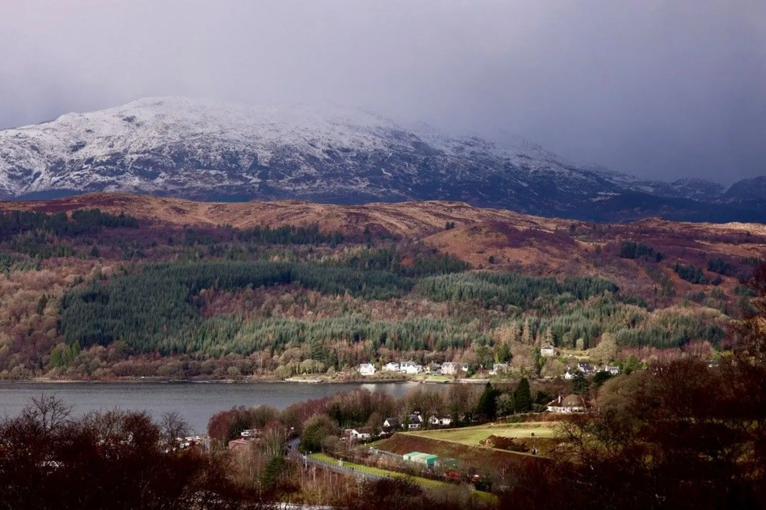 Graham Christie A snow-covered mountain range with a hill and loch below