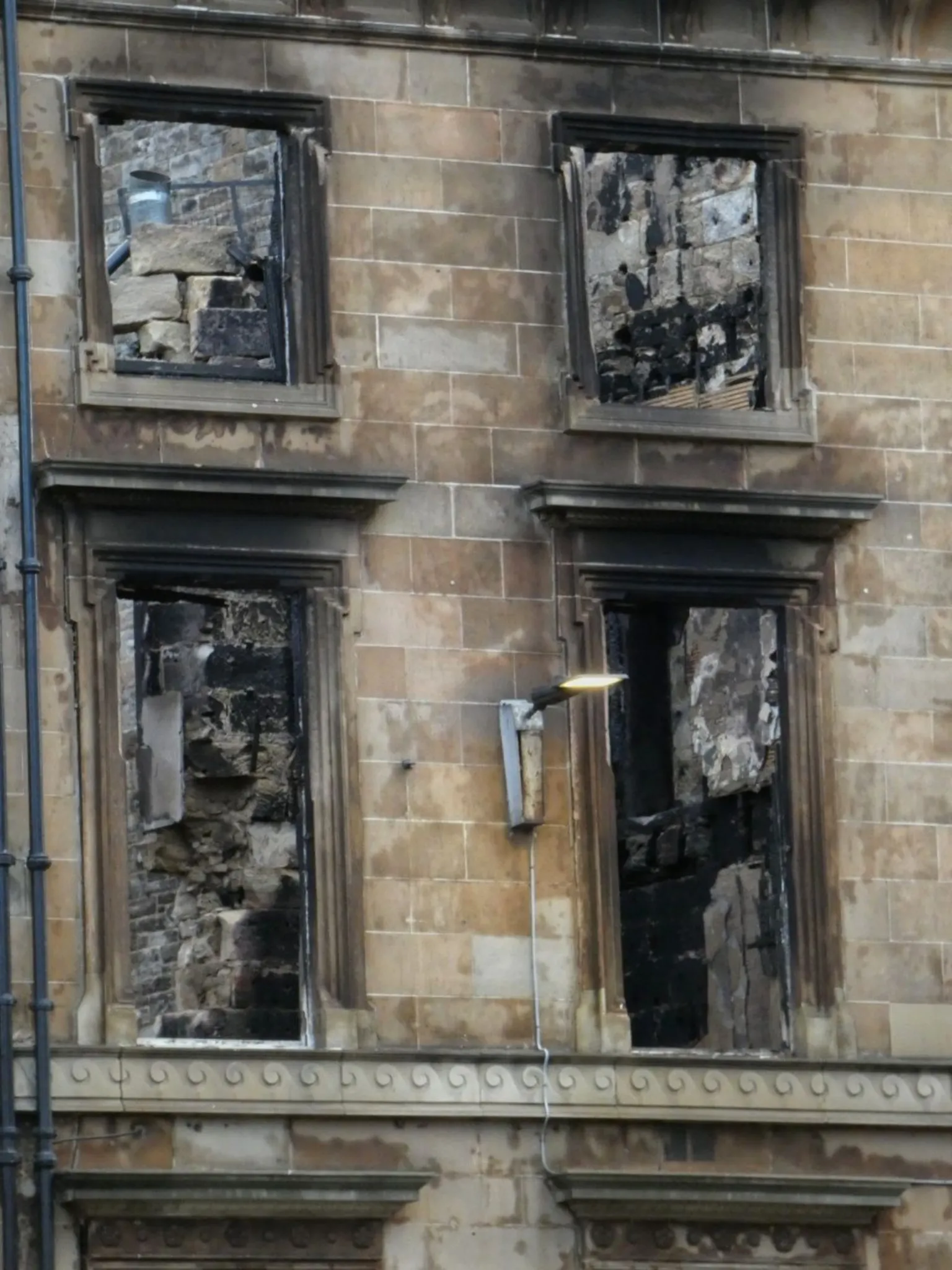 Eddie Romeo Four burned-out windows from a major fire with an illuminated street lamp attached to the building