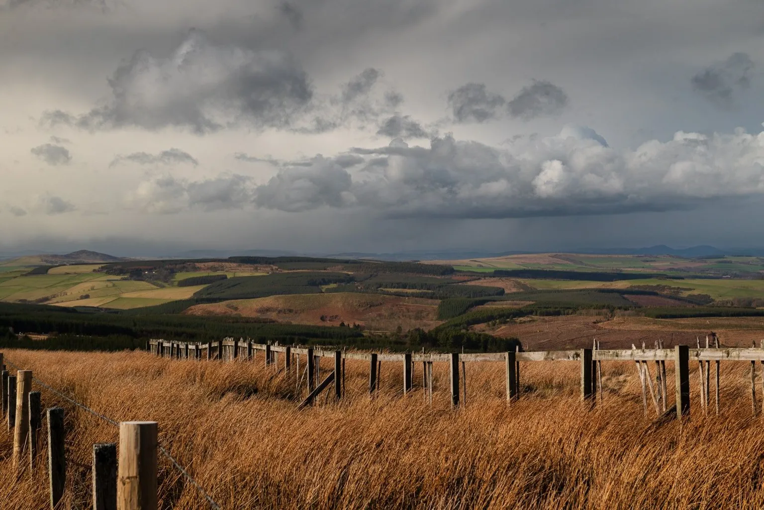 Robin Gladstone A view of fields with clouds in the sky and a fence running across the middle ground