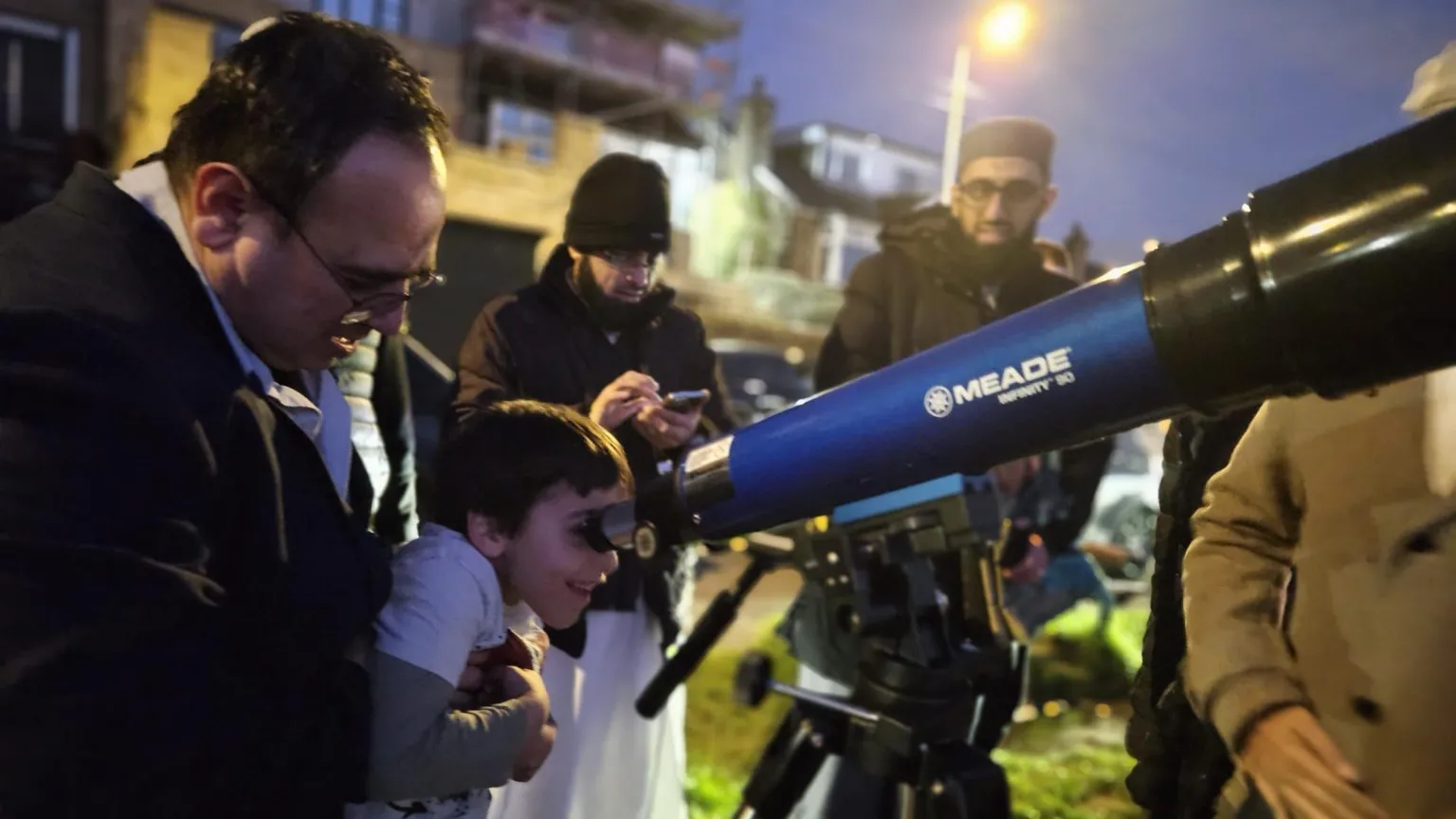 Aisha Khan/BBC A man holds a child who peers into a telescope