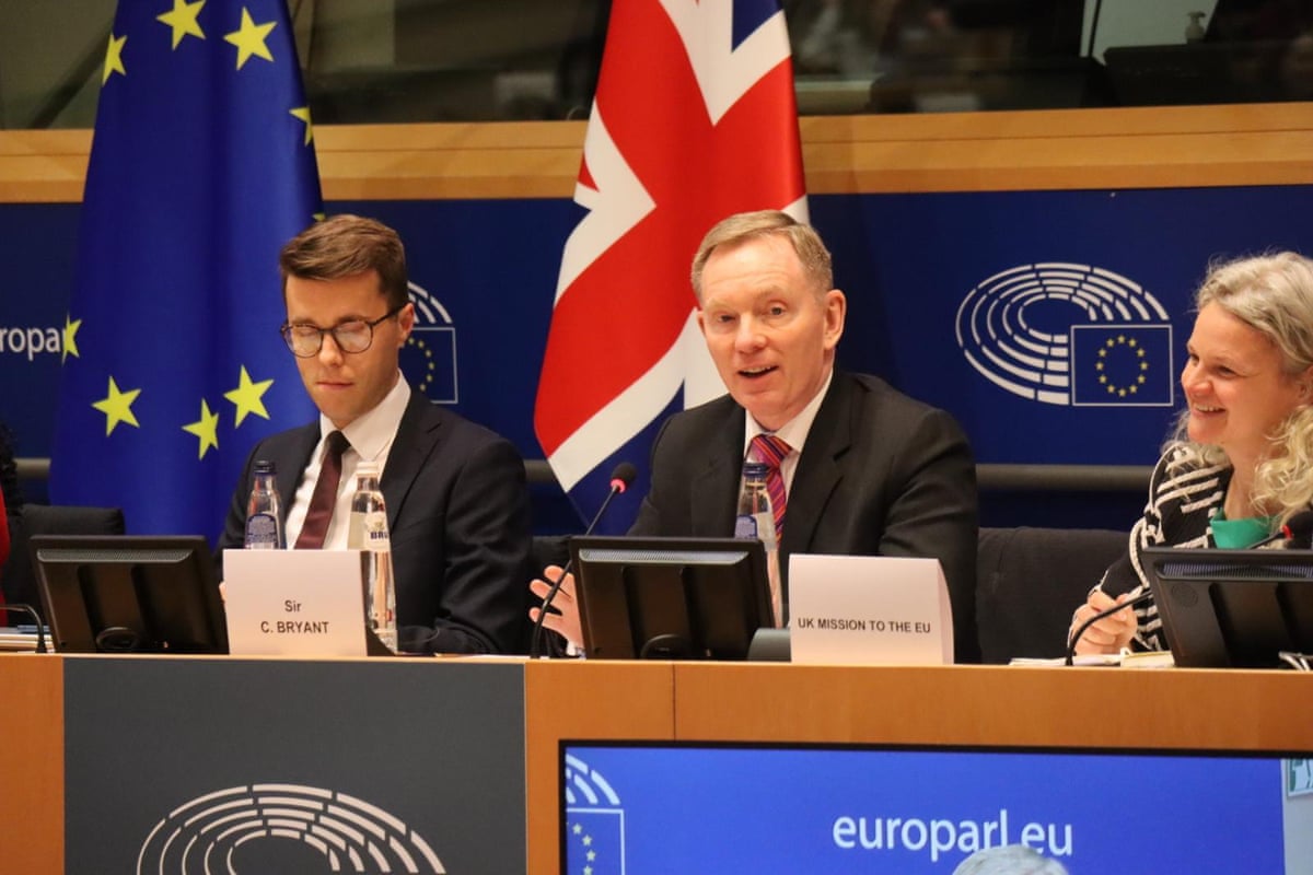 Bryant speaks at the assembly: he sits on a panel in front of a union jack flag. 