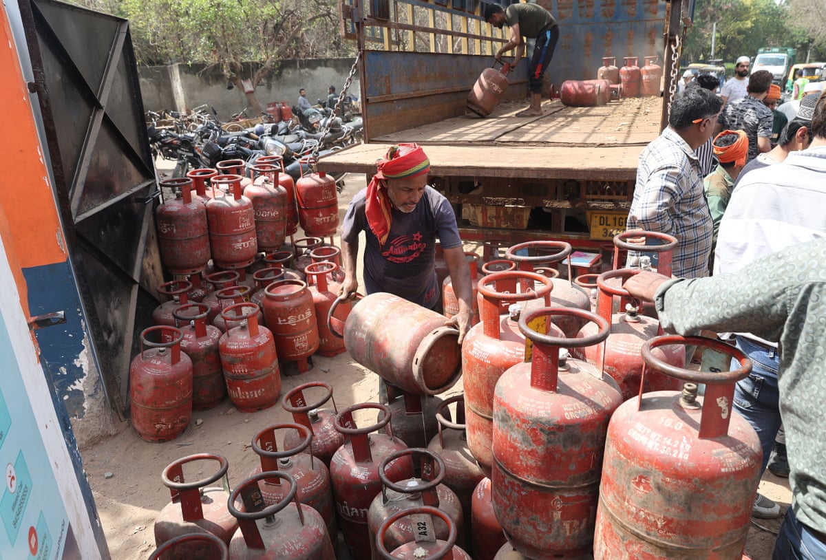 An man unloads filled LPG cylinders from a truck at a gas agency office in Delhi as people queue to the side.