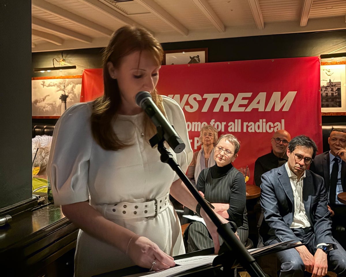Angela Rayner gives a keynote speech: she is wearing a white dress with puffed sleeves and wide belt, and stands in front of listeners and a red Mainstream banner.