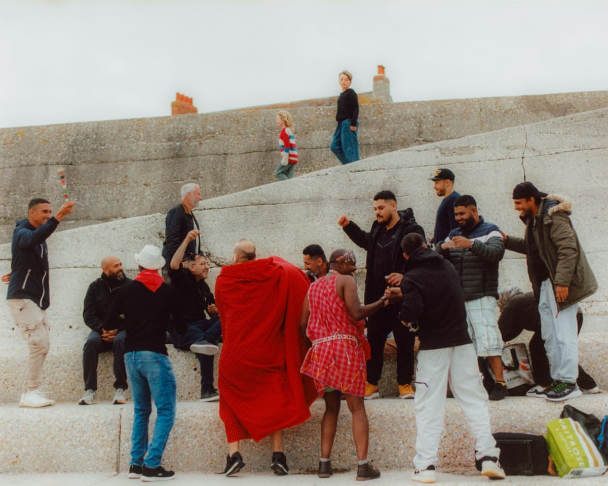 A group of men, many smiling and gesturing, on the beach