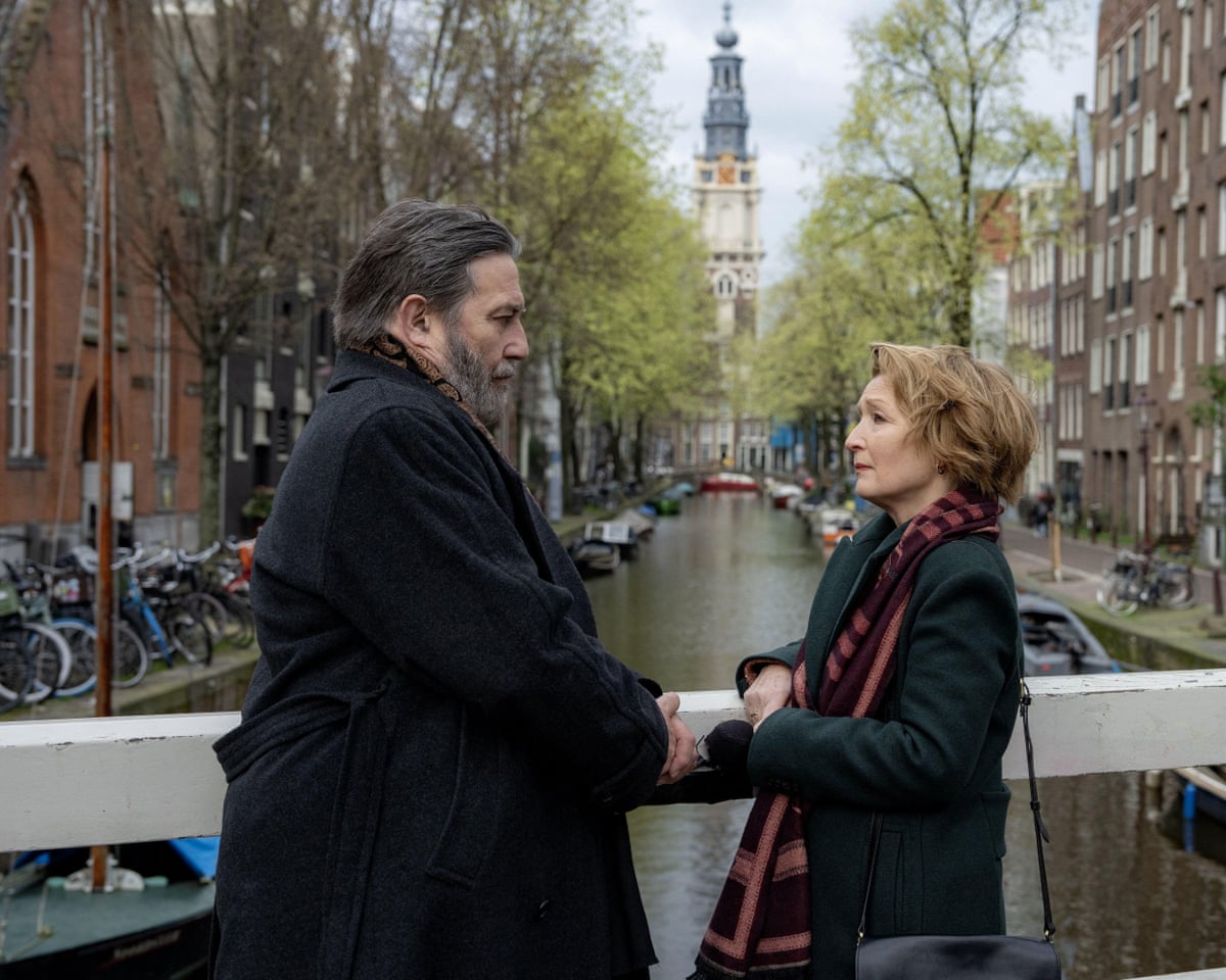 Two people standing on a bridge with buildings in the background.