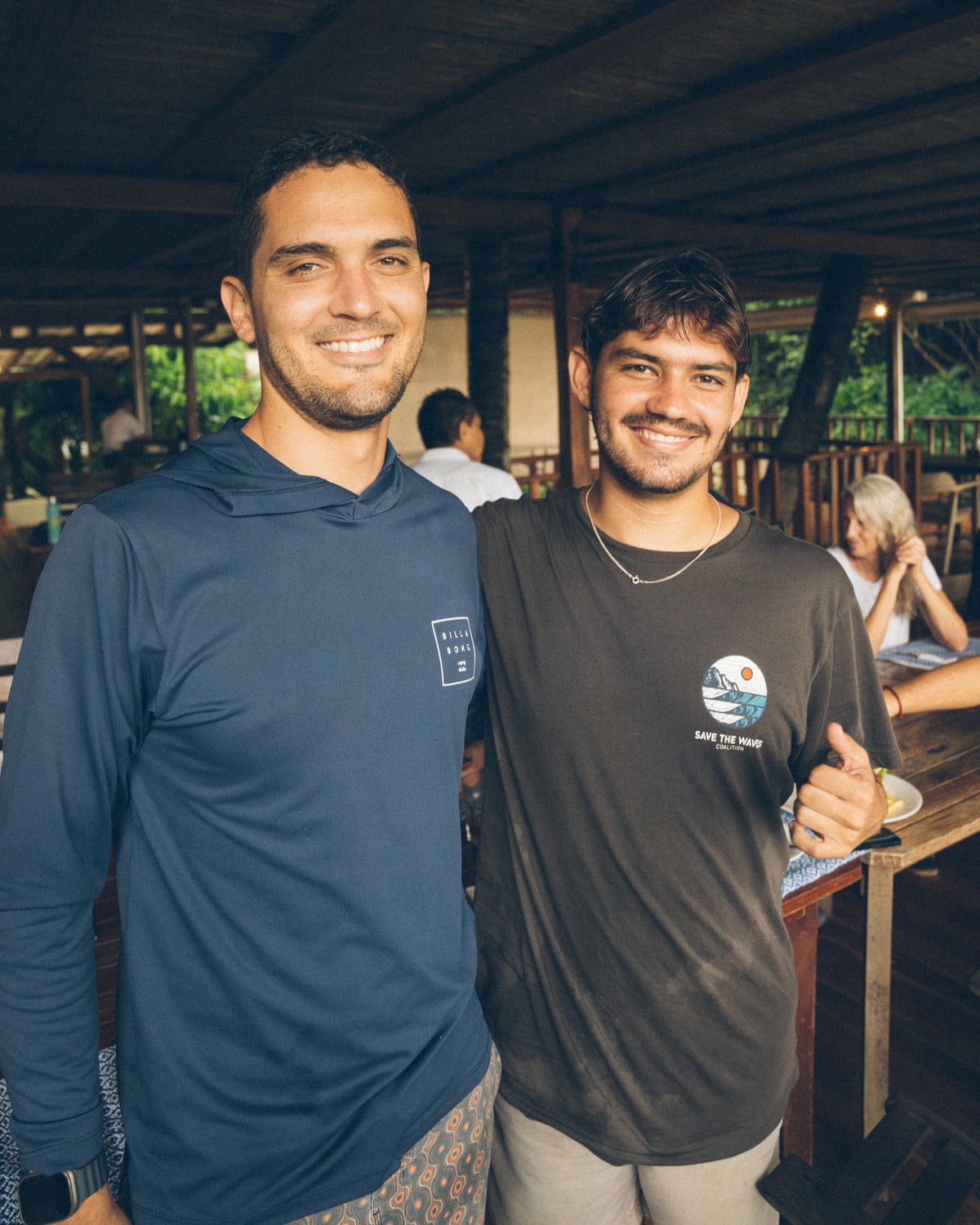 Two men stand with their arms around each other, smiling