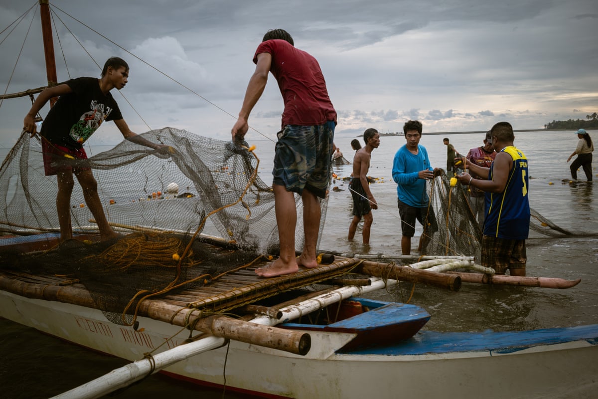 Men stand on boats and in shallow water holding fishing nets