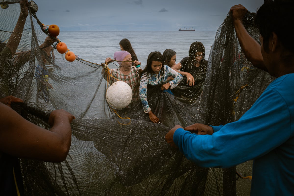 Women stand in shallow water holding up nets