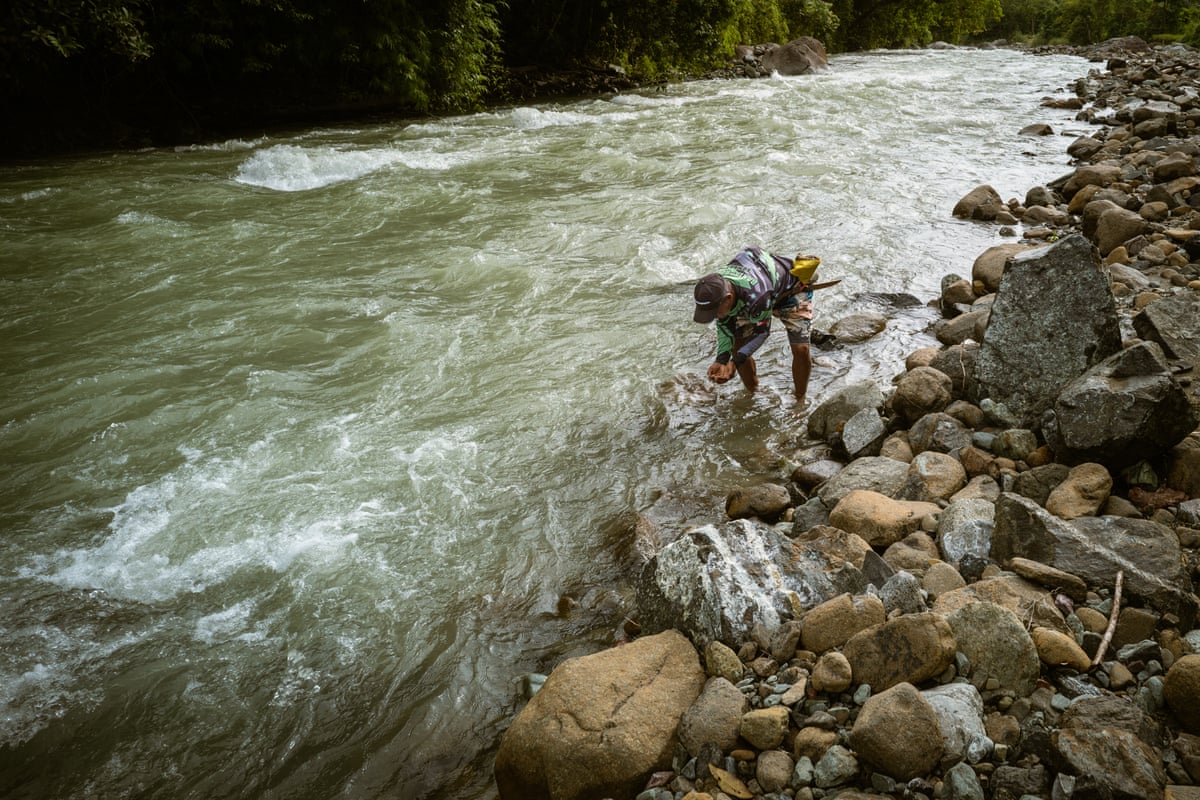 A man stands in a river and drinks from it