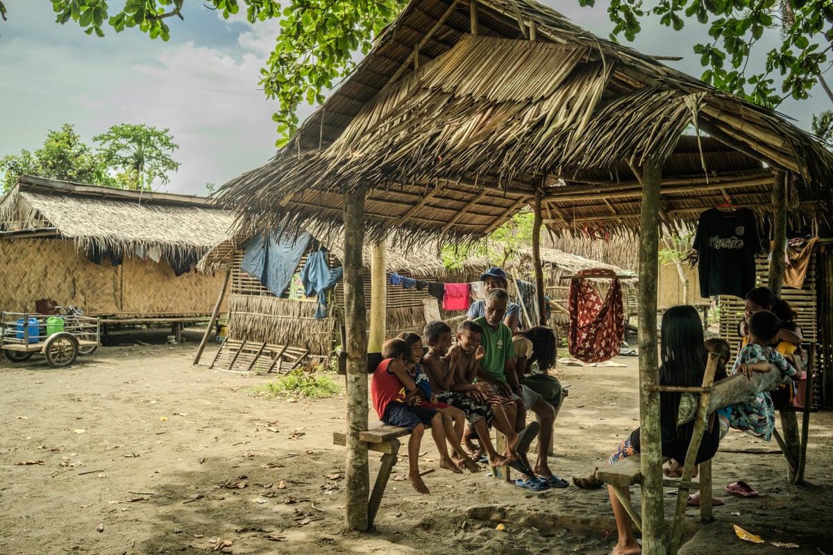 Children and adults sit on benches under a shelter