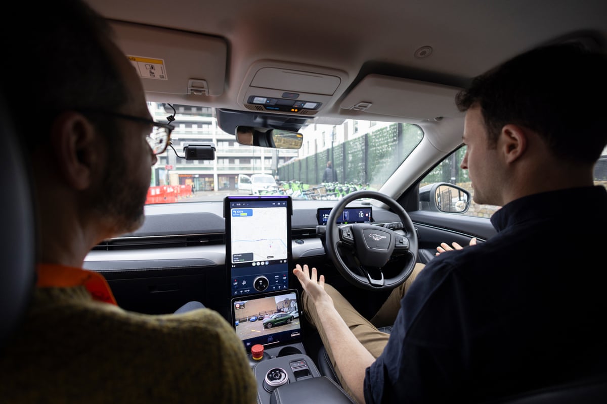 Steve Rose and Alex Kendall sit in a Wayve driverless car as it proceeds down a road in London. Kendall’s hands are not on the wheel