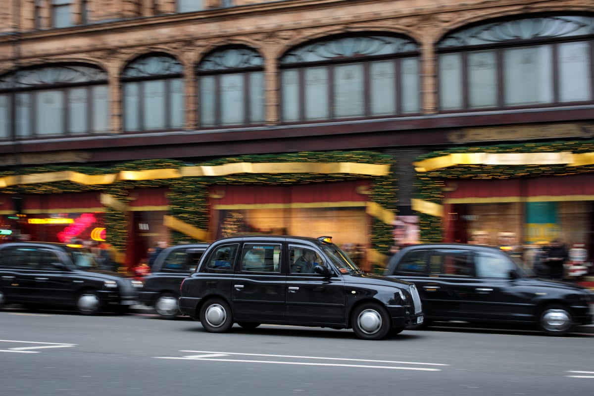 A black cab drives past a row of parked cabs outside Harrods department store in London