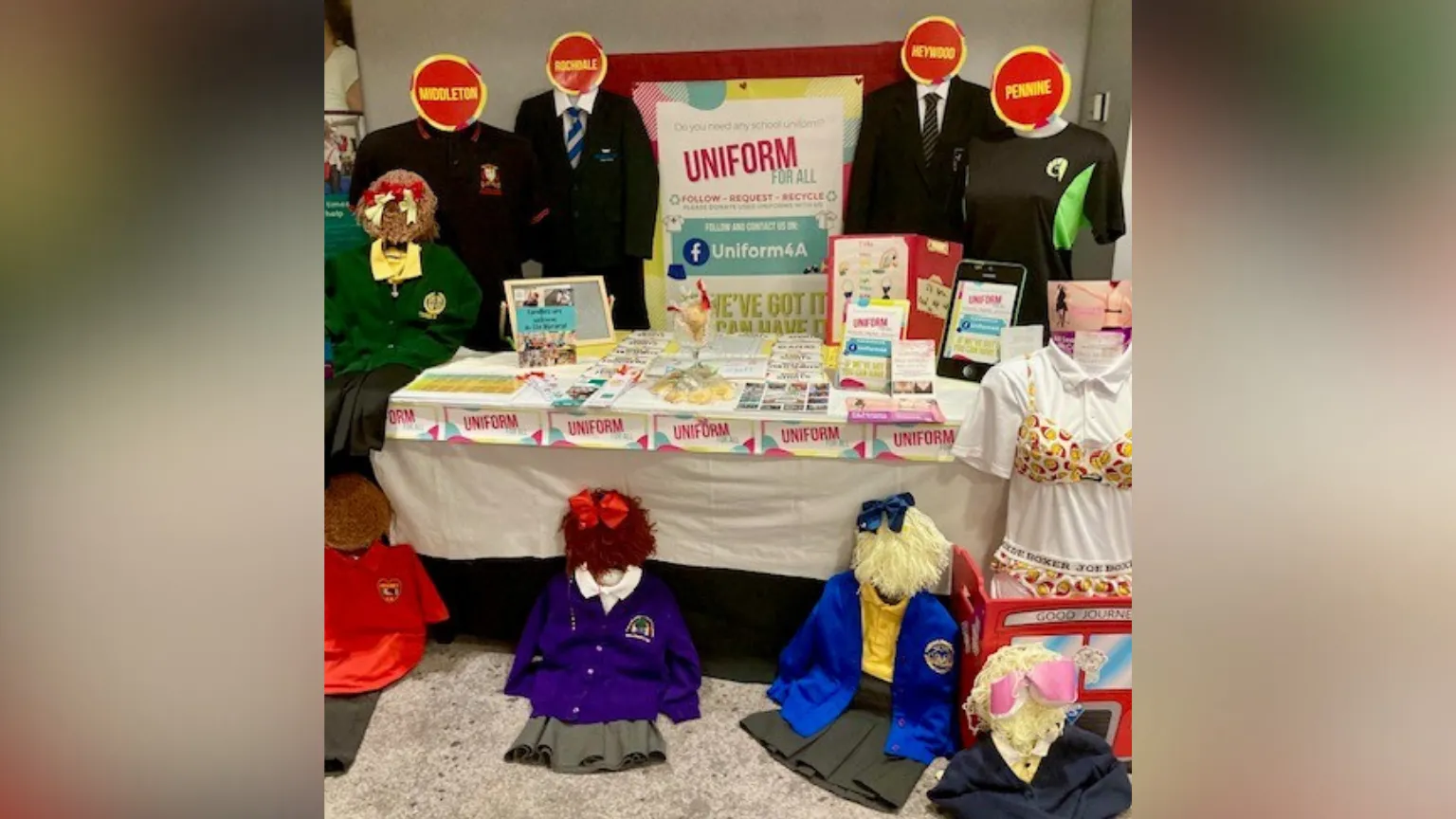 A table set up displaying different school uniforms on hangers with flyers reading 'Uniform for All'. 