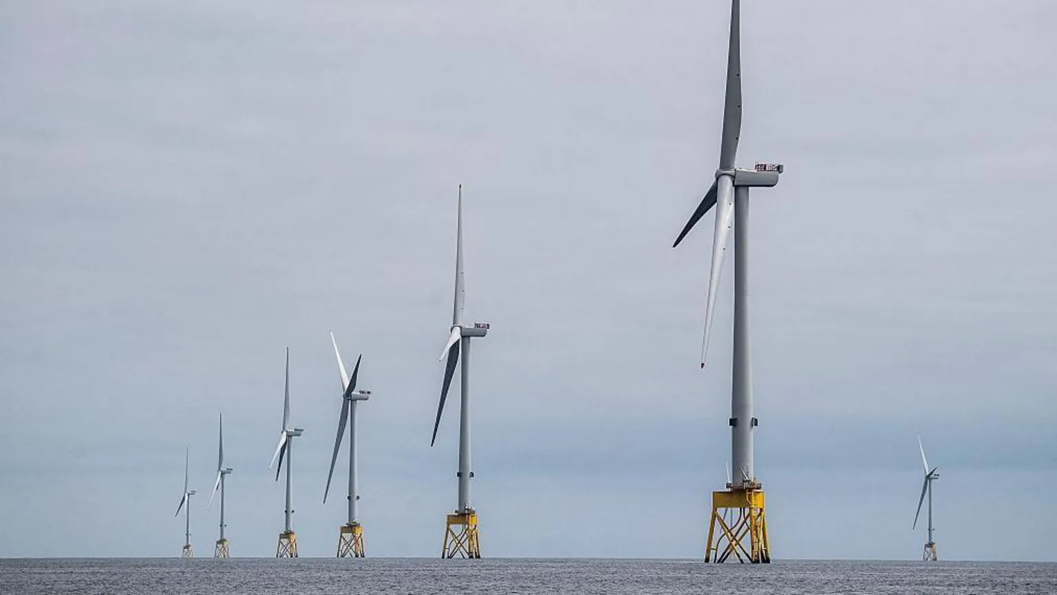 A row of wind turbines in the sea. It is very grey.