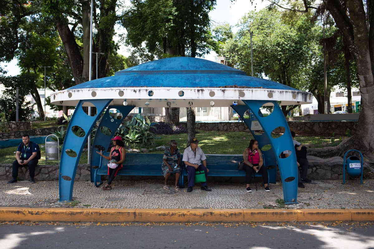 Locals wait for a bus in the shade of one of Varginha’s spaceship-shaped bus stops
