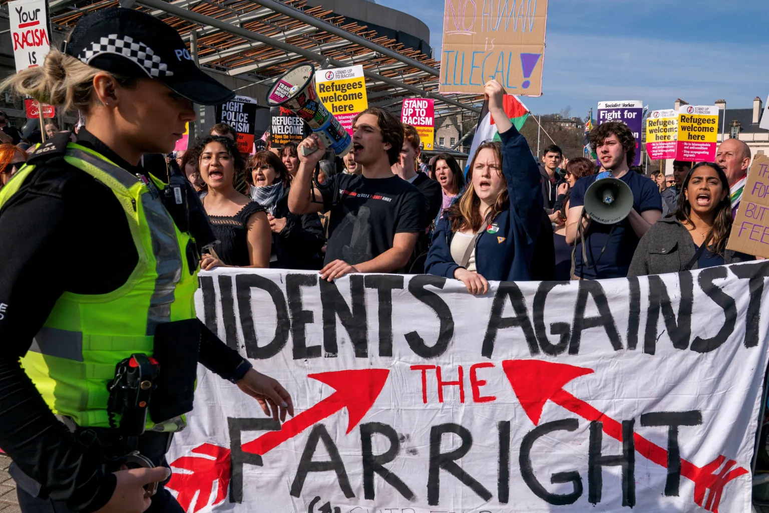 A crowd of protestors standing behind a white banner which reads: Students Against The Far Right