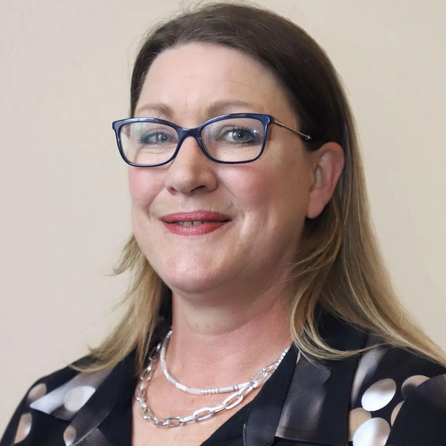 Dumfries and Galloway Council A woman with long blonde/brown hair and glasses in a black blouse with circle pattern and two silver necklaces on.