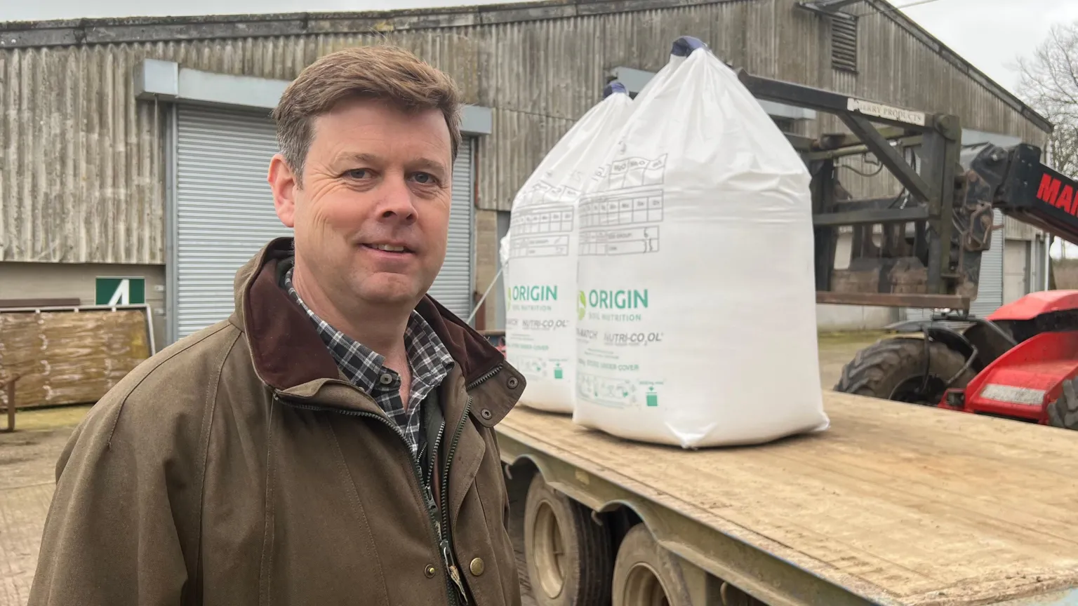 Robin Aird on a farm stood in front of a trailer with large fertiliser bags on it.