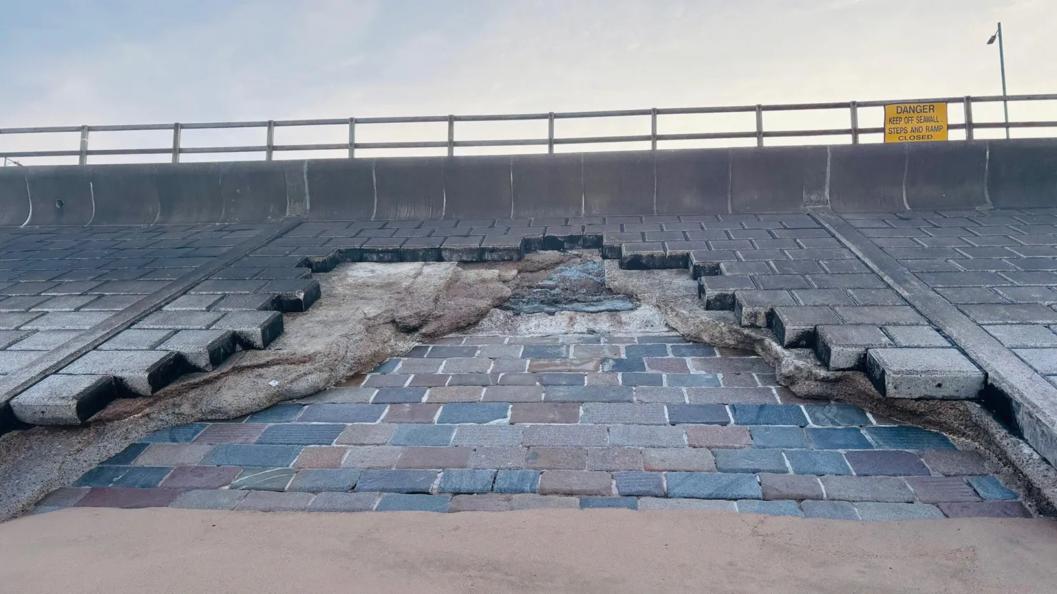 Damaged sea wall defences at Aberdeen beach, much of the stonework is missing, above the sand, and the promenade is above.