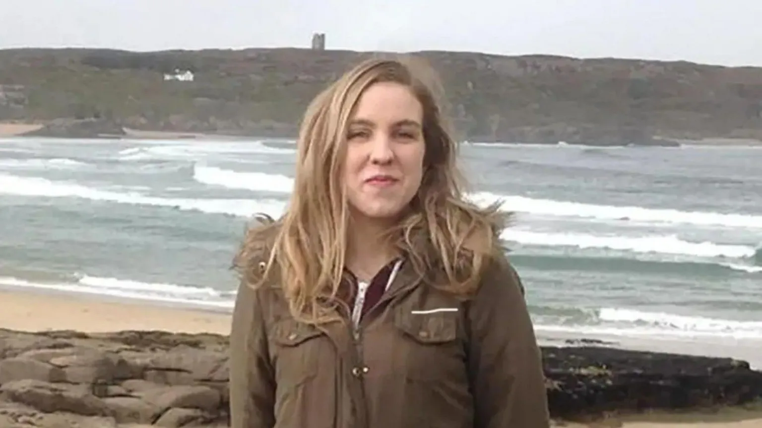 Pacemaker Natalie McNally standing on a beach with the sea visible behind her. She has long blonde hair and is wearing a dark green coat. She is smiling.